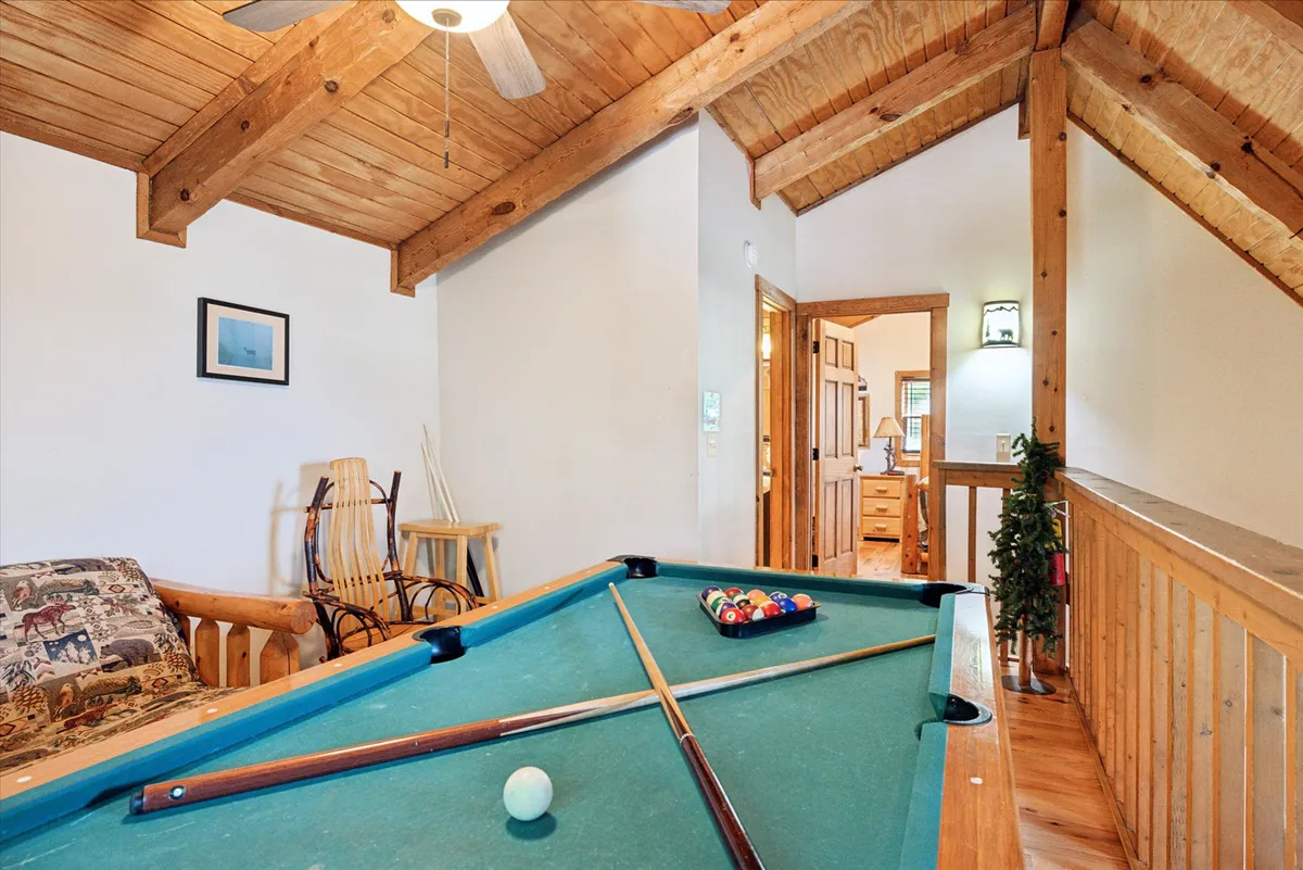 A fun, social game room space featuring a pool table, rustic wooden beams, and a cozy rocking chair. The room is designed for memorable gatherings and post-adventure relaxation, blending the warmth of the cabin with opportunities for evening entertainment.