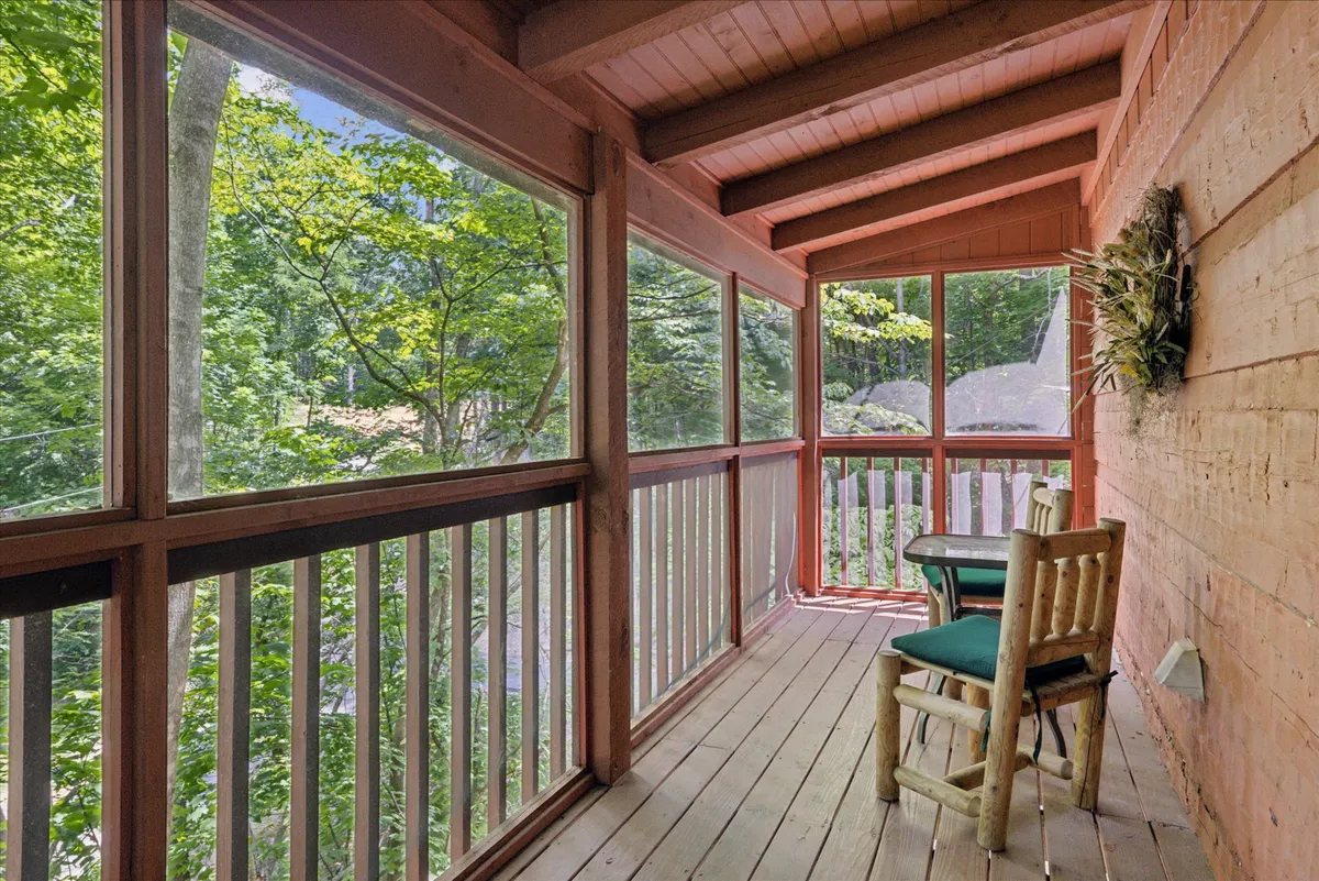 A tranquil wooden deck with green chairs and railings, adjacent to large windows. The deck is surrounded by trees, offering a calming spot to enjoy morning coffee, socialize, or simply take in the fresh mountain air.