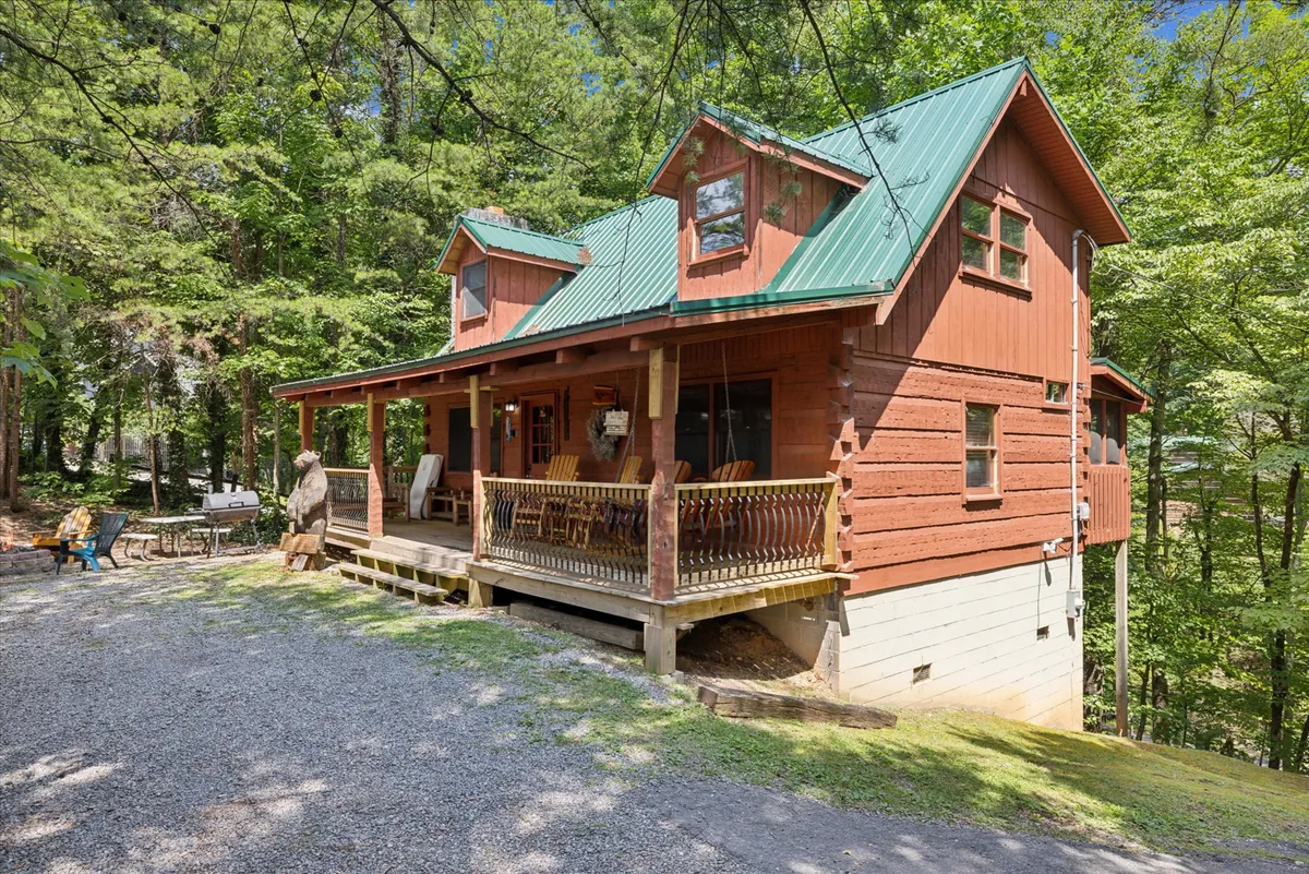 A charming wooden porch with rocking chairs beneath a green metal roof, surrounded by lush trees. The porch is ideal for relaxing, sipping coffee, or gathering with a loved one to enjoy the sights and sounds of the Smoky Mountains.