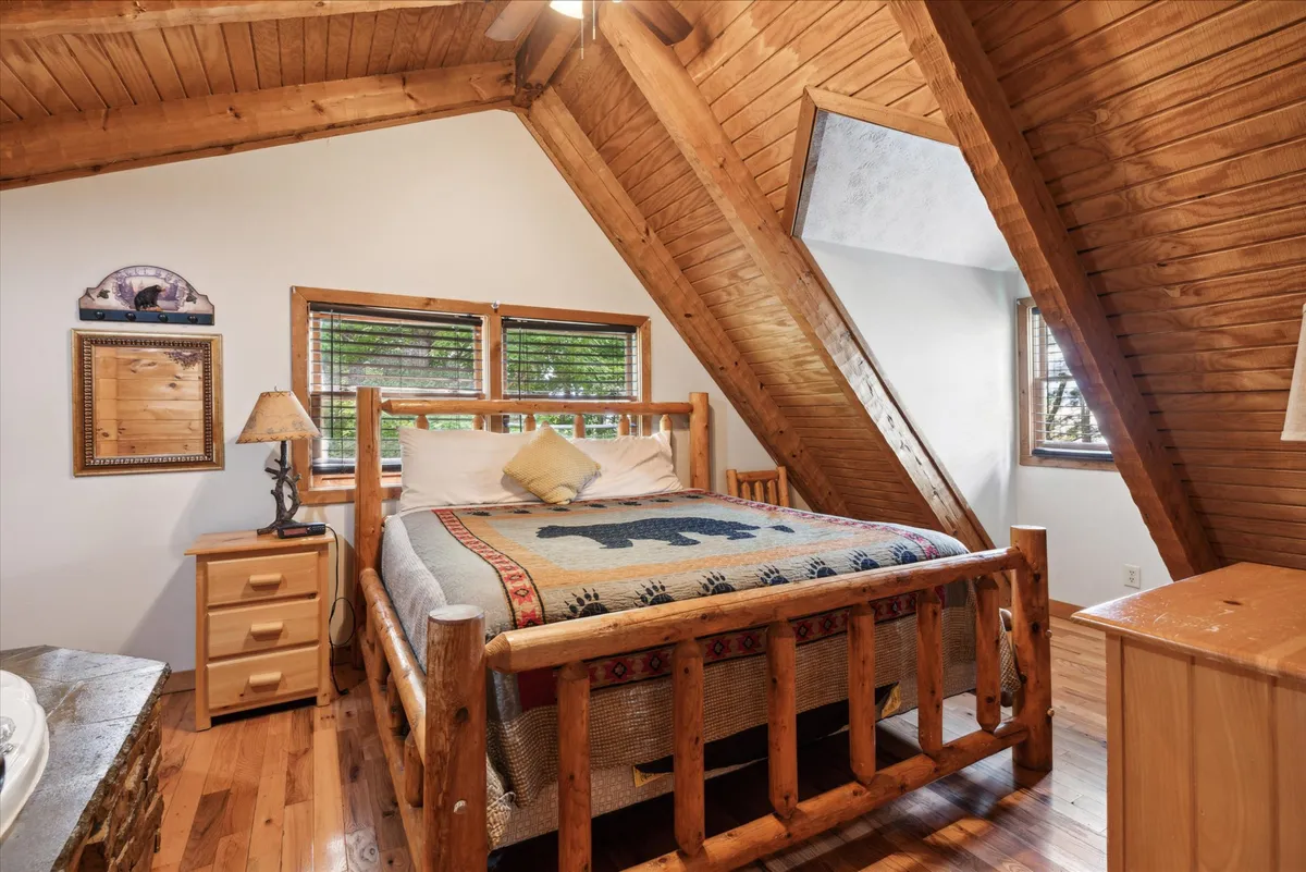 This image displays another king bedroom with a cozy log bed draped in a bear-patterned quilt, wooden furniture, and generous windows showcasing nature views. The room feels intimate and tranquil, ideal for relaxing, enjoying a good book, or simply soaking up the peaceful mountain environment.