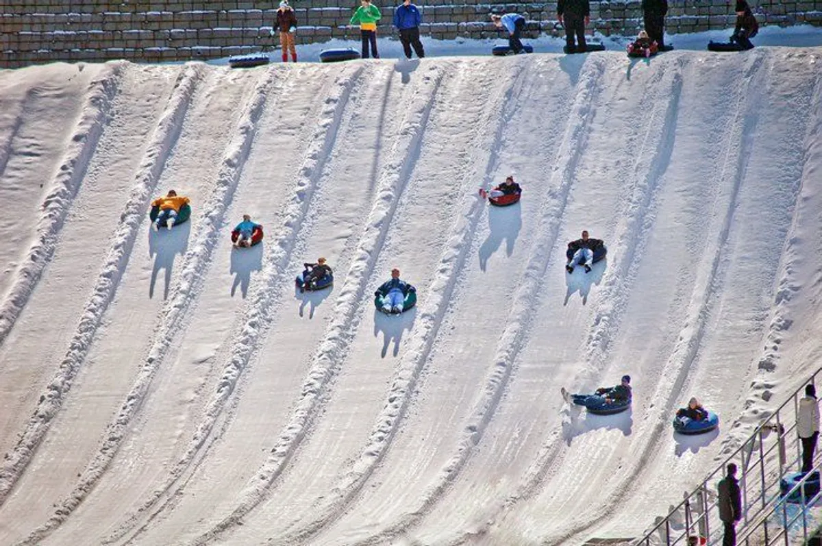 A playful winter scene featuring people sliding down a snow-covered hill with tubing equipment. Families are enjoying outdoor adventure together, surrounded by scenic mountain views and bright winter light.